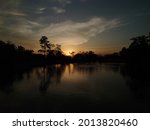 A silhouette photograph of a sunset at a lake with trees around the lakeside.
