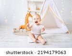 Small photo of a cute little girl is sitting in a bright cozy children's playroom. Textiles for children, for the nursery. A happy child.