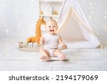 Small photo of a cute little girl is sitting in a bright cozy children's playroom. Textiles for children, for the nursery. A happy child.