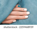 Small photo of Female hand with gems nail design. Glitter white nail polish manicure with nail art. Female model hand with perfect manicure and blue gems nail art on blue fabric background.