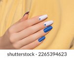 Female hand with rhinestones nail design. Glitter white and blue nail polish manicure with rhinestones nail art. Female model hand with perfect manicure and nail art on yellow fabric background.