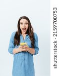 Small photo of Surprised young brunette woman holding smartphone joyfully squeals looking at camera, studio background