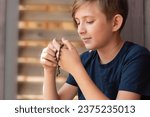 An 11 year old Catholic boy reads the rosary prayer, holds a wooden rosary with 10 beads in his hands. portrait of a boy with a wooden Catholic rosary during prayer.