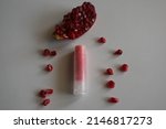 Small photo of Natural lip balms with pomegranate on white background. Lip balm or lip salve. The concept of an unnamed lipstick bottle.Commercial idea concept: Lip balm or salve and pomegranate