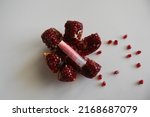 Small photo of Natural lip balms with pomegranate on white background. Lip balm or lip salve. The concept of an unnamed lipstick bottle.Commercial idea concept: Lip balm or salve and pomegranate