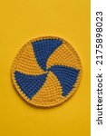 Small photo of Round blue yellow cup coaster with spiral pattern on a yellow background. Crochet coaster with tunisian pattern.