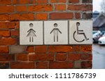 Public toilet street sign with male, female and disabled people icons on it. The sign is made of white stone mounted in the brick wall