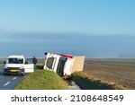 Small photo of Overturned truck in a ditch in a vast agricultural landscape while the driver is waiting for help.