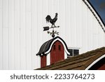 Small photo of Traditional coper rooster weathervane on a classic red barn cupola, larger white barn in background