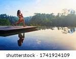 Small photo of Good morning with yoga meditating on sunrise background. Active woman in bikini practicing at villa poolside to keep fit and health. Woman fitness training, sport activity on summer family holiday.