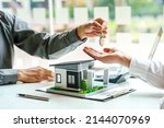 Small photo of The real estate agent gives the buyer the house keys on a table with modern miniature house model.