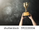 a man holding up a gold trophy cup with grunge wall background copy space ready for your trophy design.
