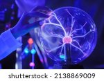 Woman hand touching plasma ball with many energy rays inside in dark room - close up view. Electricity, education, science, sci-fi, futuristic and physics concept