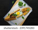 Small photo of Turkish pide or Turkish pizza flat bread and pointed at both ends filled with minced meat and toped with veges, cheese and egg or different combination. black background empty space for text.