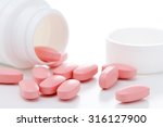 Pink oval pills poured out of a white bottle on white background.