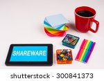 Small photo of Business Term / Business Phrase on Tablet PC - Colorful Rainbow Colors, Cup, Notepad, Pens, Paper Clips, White surface - White Word(s) on a cyan background - SHAREWARE