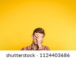 Small photo of facepalm. ashamed abashed man covering his face with hand. portrait of a young guy on yellow background popping up or peeking out from the bottom. copy space for advertising.