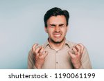 Small photo of anger rage and hatred. enraged infuriated man baring his teeth. portrait of a young brunet guy on light background. emotion facial expression. feelings and people reaction concept.