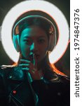 Small photo of Color light people. Cyberpunk music. Innovative technology. Noise reduction. Night portrait of blue red neon Asian girl with white halo in headphones showing shush gesture on dark.