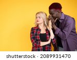 Small photo of Communication privacy. Stop rumor. Taboo topic. Forbidden secret. Multicultural couple African man gossiping hearsay to rejecting annoyed woman isolated on orange background.