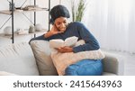 Small photo of Book leisure. Indoors weekend. Smart delighted smiling young woman enjoying reading favorite bestseller story at home resting on couch in living room interior.