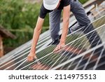 Small photo of Man technician mounting photovoltaic solar moduls on roof of house. Cropped view of builder in helmet installing solar panel system with help of hex key. Concept of alternative, renewable energy.