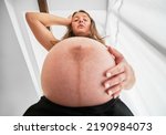 Small photo of Bottom view of pregnant lady who surprised by size of her belly. Woman putting one hand on her pregnant belly and the other on her head and looking down in dismay.
