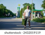 Small photo of Confident man finally found petrol station and fill canister. Man returning to car to refuel it. Young male with canister in hand on background of gas station.