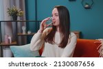 Small photo of Close-up portrait of young woman sitting on sofa at home holds glass drinks water, makes gulp of clean aqua reducing thirst caring about health and beauty. Healthy girl lifestyle, enough liquid intake