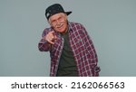 Small photo of Amused senior man in casual shirt pointing finger to camera, laughing out loud taunting making fun of ridiculous appearance, funny joke. Elderly grandfather posing alone on gray studio wall background