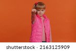 Small photo of Angry aggressive toddler children girl showing fig negative gesture, you dont get it anyway. Rapacious, avaricious, acquisitive. Body language. Refusal fig sign. Greedy child kid on orange background