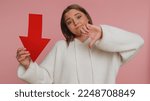 Small photo of Upset young woman showing red arrow pointing down, concept of downgrade, unsuccessful business, fall of stock market money exchange rate, bankruptcy fail. Sad girl isolated on pink studio background
