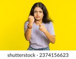 Small photo of Aggressive angry Indian young woman trying to fight at camera, shaking fist, boxing with expression, punishment, threaten, bullying, abuse, mad fury. Arabian girl isolated on yellow studio background