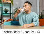 Small photo of Thirsty Asian man hold glass of natural filtered aqua make sips drinking still water preventing dehydration at home. Water after reverse osmosis filter. Guy with good life habits, healthy, weight loss