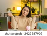 Small photo of Poor Caucasian young woman insufficient amount of money, holding piggybank and one dollar banknote. Financial crisis. Bankruptcy. Poverty and destitution. Female girl sitting at home room at table