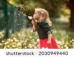 Portrait of happy girl. Child is smiling in spring day. Kid is enjoying spring. Sunny day. Blonde girl is blowing dandelion. Outdoor, close up.