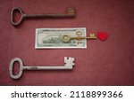 Small photo of Love money. A heart surrounded by old keys on a burgundy background, one golden key closer to the heart lies on a hundred dollar bill. Be closer to the dream! Valentine's Day