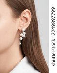 Small photo of Close-up shot of a girl with smooth long brown hair and natural makeup. The accent is on the ears with an elegant twig stud earring decorated with artificial pearls.