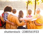 Small photo of A multiethnic group of friends, bound by love and adventure, stand united by a forest lake. As the sun casts a golden farewell, their close embrace mirrors the days warm memories. Their backpacks tell