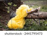 Small photo of A tranquil scene unfolds as a woman in a luxurious yellow gown finds repose on a fallen tree amidst the serene forest floor, blending restfulness with natural grandeur. Repose in Nature: Woman in a