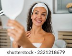 young girl with headband in a spa looks at herself in a mirror and she's happy with her spa treatment