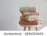 Small photo of Stack of clean freshly laundered, neatly folded women's clothes on wooden table. Pile of shirts, dresses and sweaters on the table, white wall background. Copy space, close up, top view.