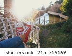 Cropped shot of female feet lying on the net hammock on the country house yard. Legs of a woman wearing blue jeans and red white snickers, relaxing on a beautiful day. Close up, copy space, background