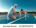 Small photo of Instructor and athlete runner on the track. The athletics marks the time in the plank exercise on a stopwatch. Fitness trainer and mentee.