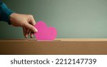 Small photo of Donation Concept. Hand Droping a Pink Paper Heart into a Donate Box. Helping, Supporting and Togetherness. Side View