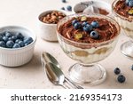 Traditional Italian dessert tiramisu with blueberries in glass. Individual trifle. Homemade layered cake with berries in cup. Selective focus.