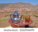 Small photo of Tea pot with glasses on colorful tray, Ourika valley and High Atlas Mountains in the background. Morocco. High quality photo