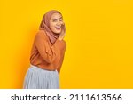 Small photo of Beautiful young Asian woman in brown sweater and hijab hand on mouth telling secret, whispering gossip, looking at camera with cheerful expression on yellow background. People islam religious concept