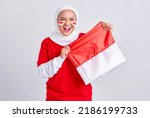 Smiling young Asian muslim woman in red white t-shirt celebrating indonesian independence day on 17 august with proudly to showing flag indonesian isolated on white background