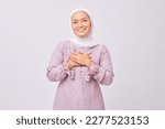 Portrait of smiling beautiful young Asian Muslim woman wearing hijab and purple dress holding hands on chest and greeting welcoming Ramadan isolated on white studio background